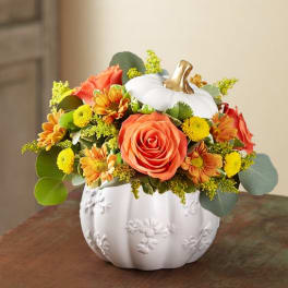 Orange roses and yellow flowers arranged in a white pumpkin vase