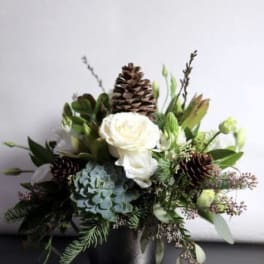 White roses and blue hydrangea in a black vase with pinecones