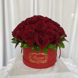 Red rose arrangement in a round red box with gold lettering