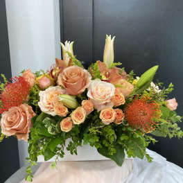 Peach roses and orange pincushion blooms in a white rectangular vase