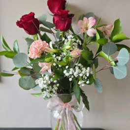 Bouquet of red roses and pink flowers in a glass vase with a ribbon