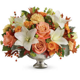 Orange roses and white lilies arranged in a silver pedestal vase