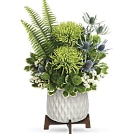 Green floral arrangement in a white textured vase on a wooden stand