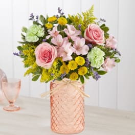 Pink roses and pastel flowers arranged in a peach glass vase