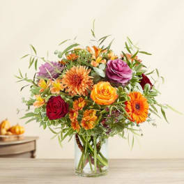 Mixed bouquet of orange, red, and purple flowers in a clear glass vase