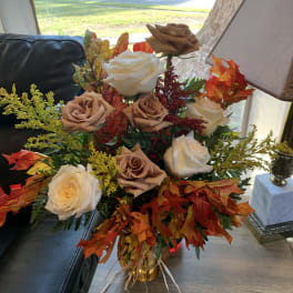 Bouquet of cream and tan roses with autumn leaves in a glass vase