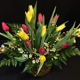 Low arrangement of yellow and red tulips with small white blossoms in a clear glass bowl