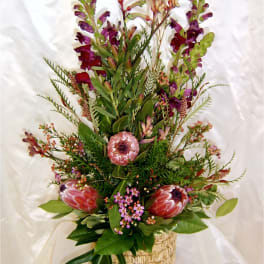 Tall floral arrangement with pink protea and purple snapdragons in a woven basket
