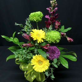 Mixed bouquet with yellow gerbera daisies, green chrysanthemums, and purple blooms in a vase