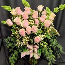 Pink roses arranged in a glass vase with greenery and a pink ribbon