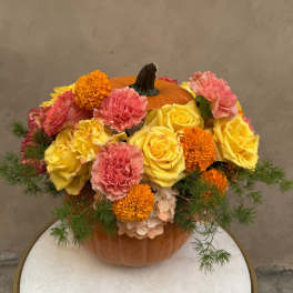 Pumpkin centerpiece with yellow roses, pink carnations, and orange marigolds