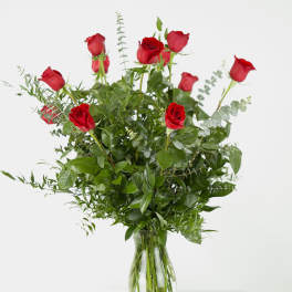 Red roses arranged in a clear glass vase with mixed greenery