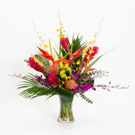 Tropical flower arrangement in a clear glass vase with red, orange, yellow, and purple blooms