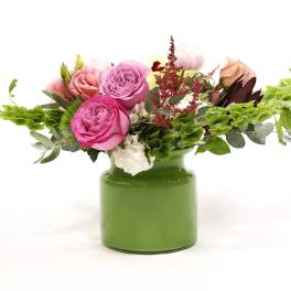 Pink and peach roses in a green vase with trailing greenery