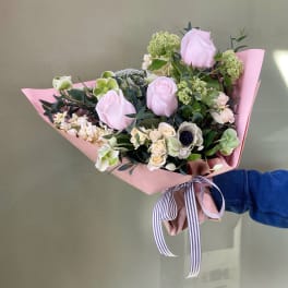 Handheld bouquet of pale pink roses and mixed blooms wrapped in pink paper