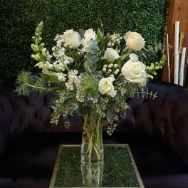 White roses and mixed greenery arranged in a clear glass vase.