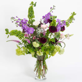 Tall mixed bouquet of purple, white, pink, and green flowers in a clear glass vase