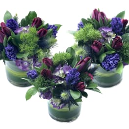Three purple floral arrangements in green glass vases