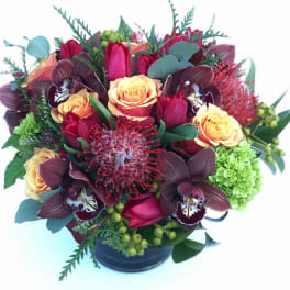 Bouquet of red tulips, peach roses, and dark orchids in a black vase
