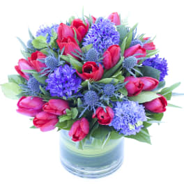 Bouquet of red tulips and purple flowers in a glass vase