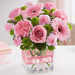 Pink roses and gerbera daisies in a clear square vase with a ribbon