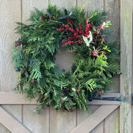 A green holiday wreath with red berries hangs on a wooden door.