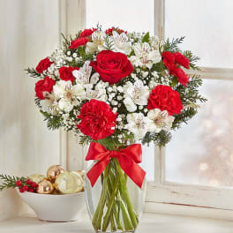 Red and white flower bouquet in a clear glass vase with a red ribbon.