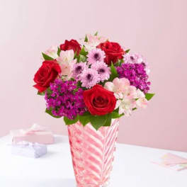 Red roses and pink flowers in a striped glass vase