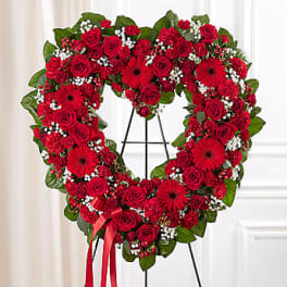 Heart-shaped red rose and gerbera wreath on a stand with ribbon
