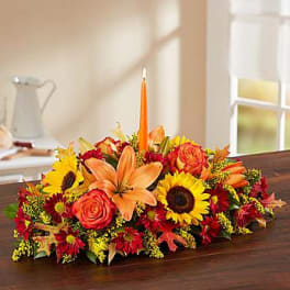 Low floral centerpiece with lilies, roses, and sunflowers around a candle