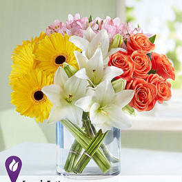 Bouquet of yellow gerbera daisies, white lilies, and orange roses in a glass vase