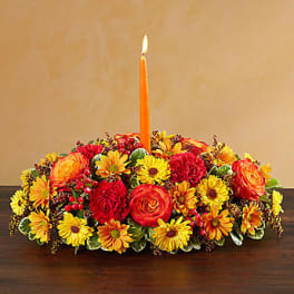 Low floral centerpiece with a lit orange taper candle