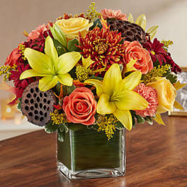 Mixed bouquet of yellow lilies, coral roses, and red mums in a glass vase