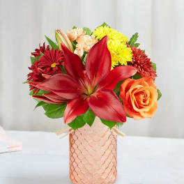 Bouquet of red lilies, roses, and yellow chrysanthemums in a pink vase
