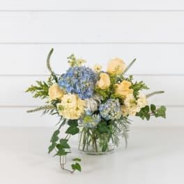 Blue hydrangeas and pale yellow roses in a clear glass vase