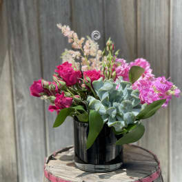 Pink roses and carnations arranged with a succulent in a black vase