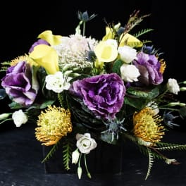 Purple and yellow floral arrangement with white blooms in a black container
