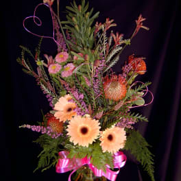 Tall mixed bouquet with peach gerberas, pink blooms, and a pink ribbon in a glass vase