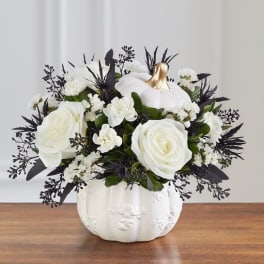 White roses and small white flowers in a white pumpkin vase