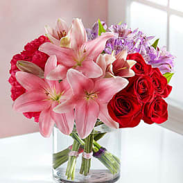 Bouquet of pink lilies and red roses in a clear glass vase