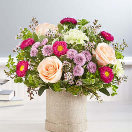 Peach roses and pink daisy-like flowers in a burlap-wrapped container