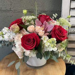 Mixed bouquet of red roses, pink lilies, and white blooms in a white vase