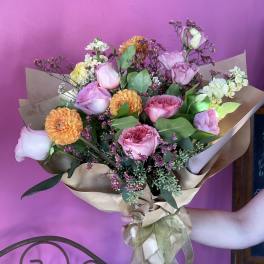 Bouquet of pink roses and orange dahlias wrapped in brown paper