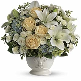 Cream roses and white lilies arranged in a white urn vase