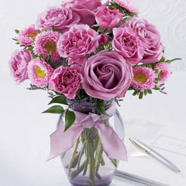 Pink roses and daisies arranged in a glass vase with a ribbon