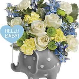 White and blue flowers in a gray elephant planter with a "Hello Baby!" sign