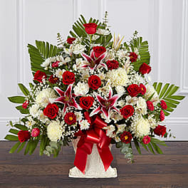 Large red and white floral spray in a white pedestal vase with a red ribbon