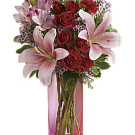Bouquet of red roses and pink lilies in a tall pink glass vase