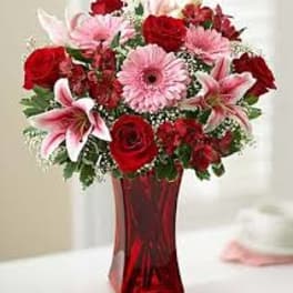 Red and pink mixed flower arrangement in a red glass vase