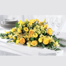 Yellow floral centerpiece on a white table with plates and wine glasses